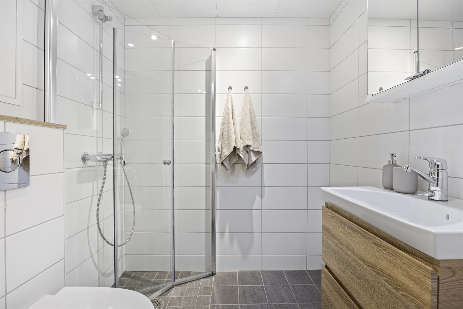 Lekkert en-suite bad med adkomst fra hovedsoverom. Flislagt bad med gulvvarme. Vegghengt toalett og heldekkende servant med underskap, overskap med speil og lys, samt dusjsone med innfellbare dører i glass. Himlingsplater i stål med integrerte downlights Galleribilde