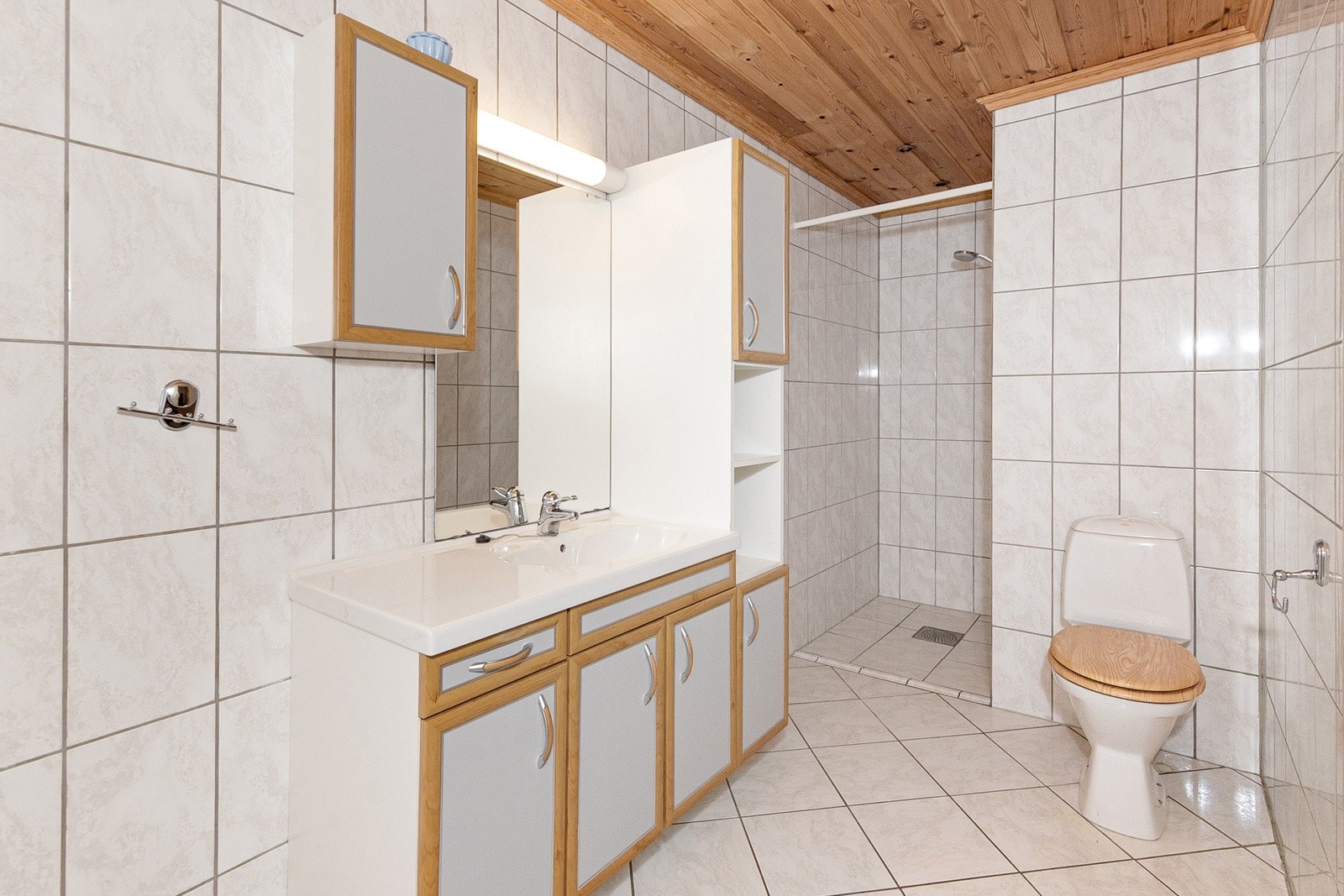 Vegghengt høyskap og servantskap. Speil, skap og overlys med stikkontakt på vegg over servant. Badekar og dusjnisje. Galleribilde