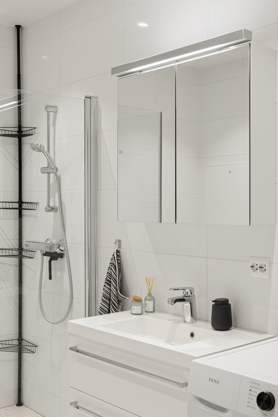 Hvit baderomsinnredning med heldekkende servant og speilskap med tilhørende belysning. Galleribilde