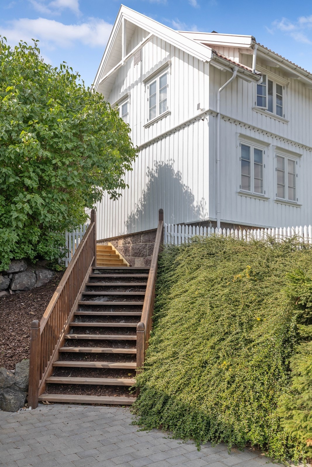Trapp i treverk fører opp til inngangspartiet og hagen, omkranset av grøntområder. Galleribilde