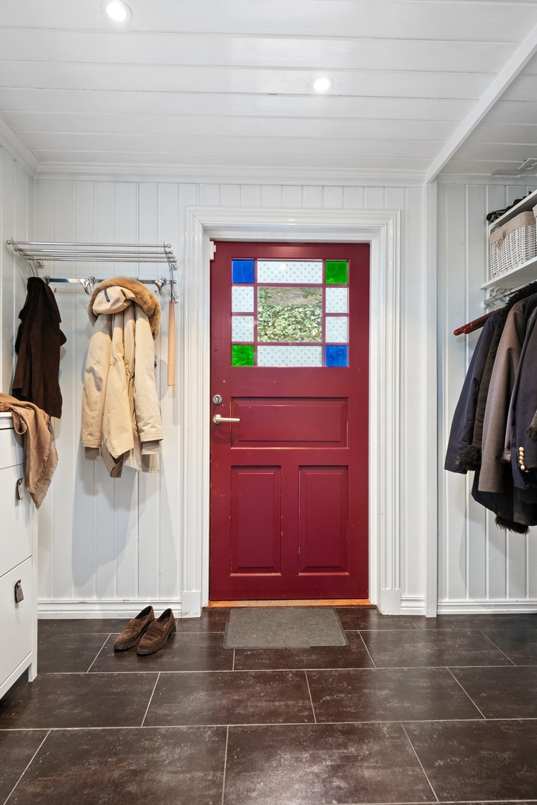 Entré med flislagt gulv og en rød dør med dekorativ glass, samt god plass til oppheng av klær. Galleribilde
