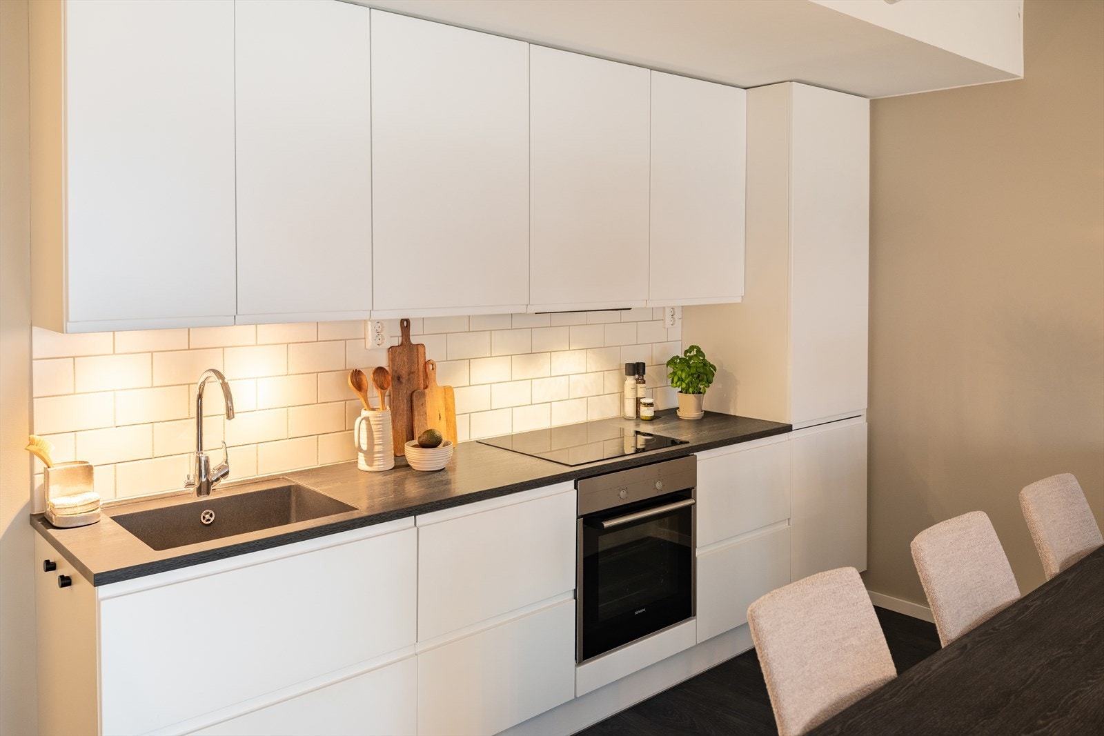 Pent kjøkken i takhøy utførelse og slette fronter. Her er det integrerte hvitevarer som stekeovn, platetopp, kombiskap, oppvaskmaskin og ventilator. Galleribilde