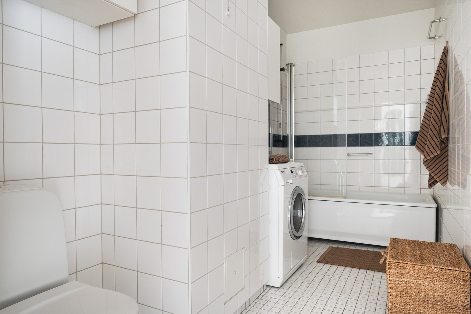 Flislagt baderom med elektriske varmekabler. Badet er innredet med badekar med dusjvegg, gulvstående toalett og enkel servant. Det er opplegg for vaskemaskin. Plastluk under badekar. Galleribilde