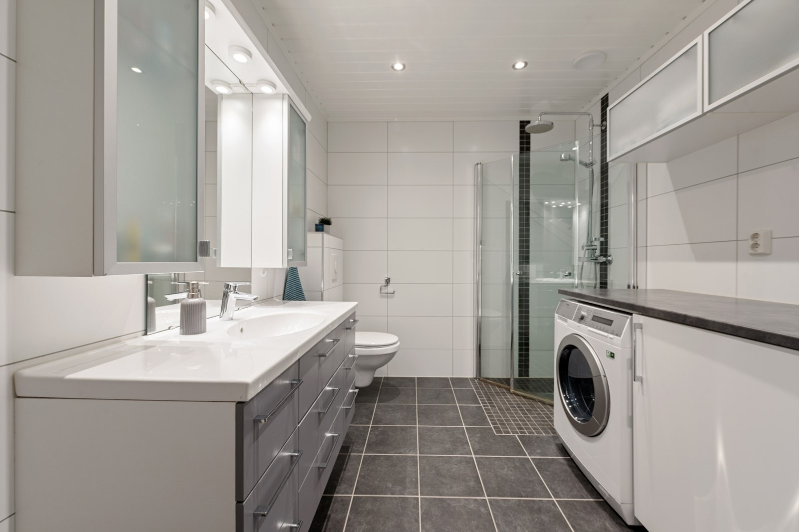 Badet har praktisk vaskeromsløsning med opplegg for vaskemaskin, benk og skap for ekstra oppbevaring på badet Galleribilde