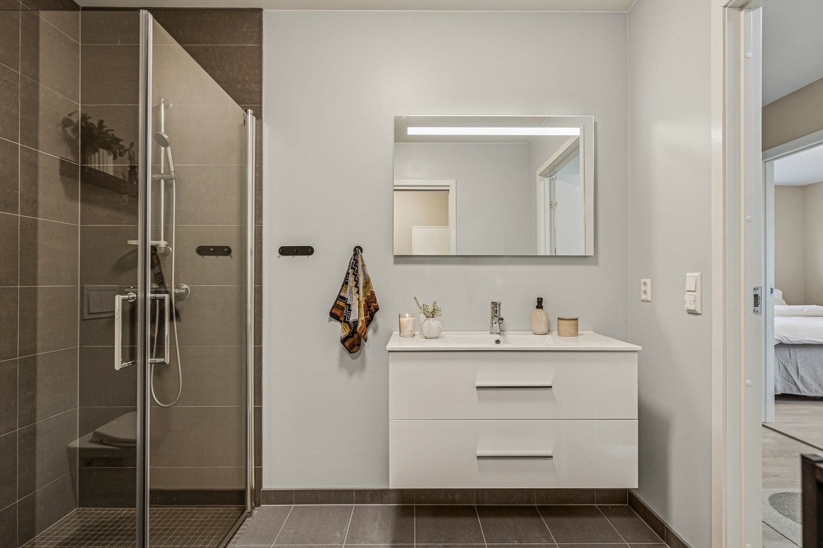 Dusjhjørne med glassvegger, vegghengt toalett og moderne servantinnredning gir et gjennomført og elegant uttrykk. Galleribilde