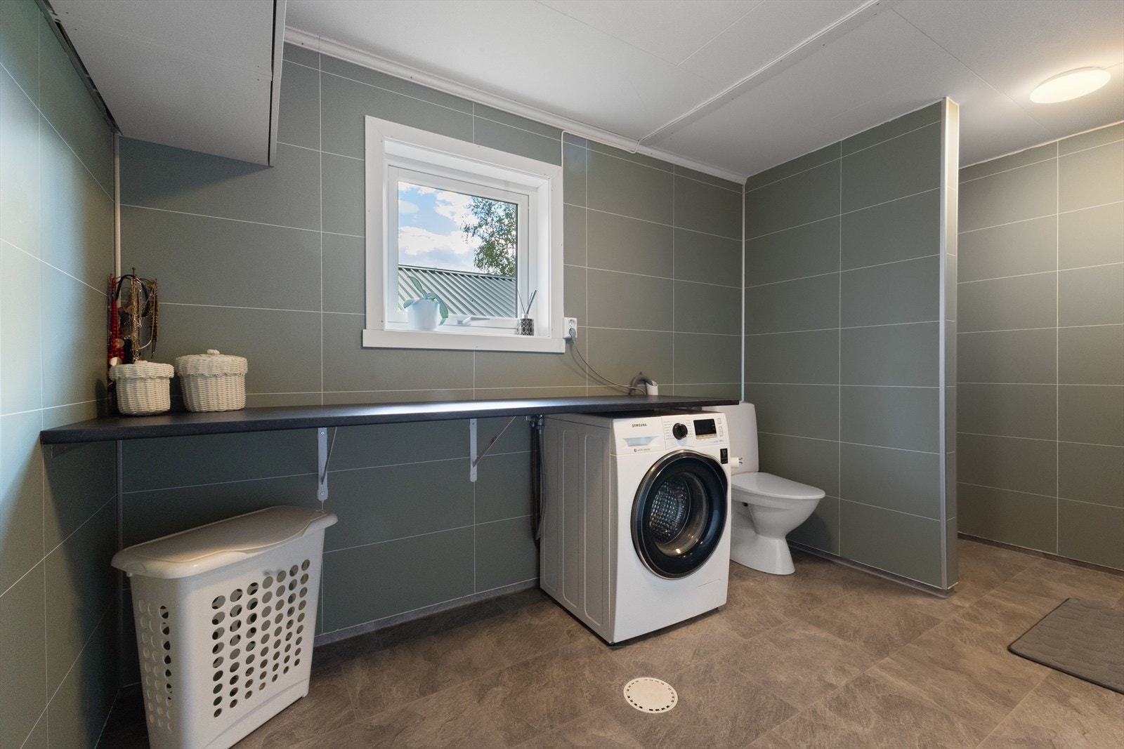 En praktisk arbeidsbenk er montert over vaskemaskinen. Dette gjør det lettvint å brette klær når de er tørre. Galleribilde