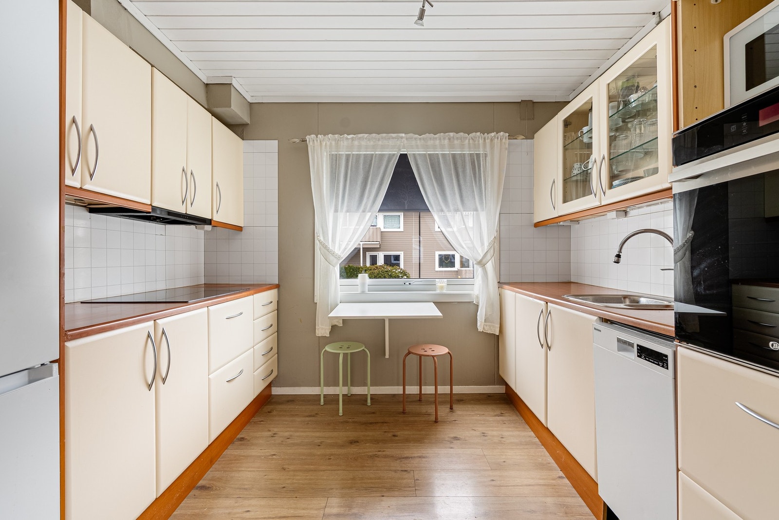 På kjøkkenet videreføres helheten med samme gulv og malt panel i taket, samtidig som rommet er tydelig definert med mørkere vegger og kjøkkenplater som gir kontrast og karakter Galleribilde