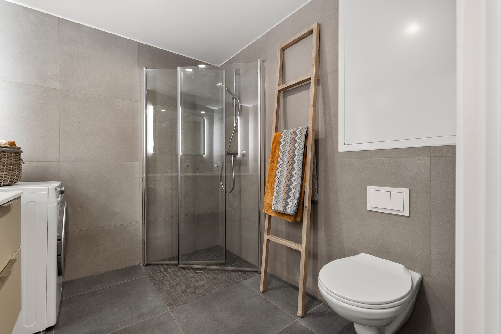 Badet er utstyrt med vegghengt klosett, dusjdører, servant samt opplegg til vaskemaskin. Galleribilde