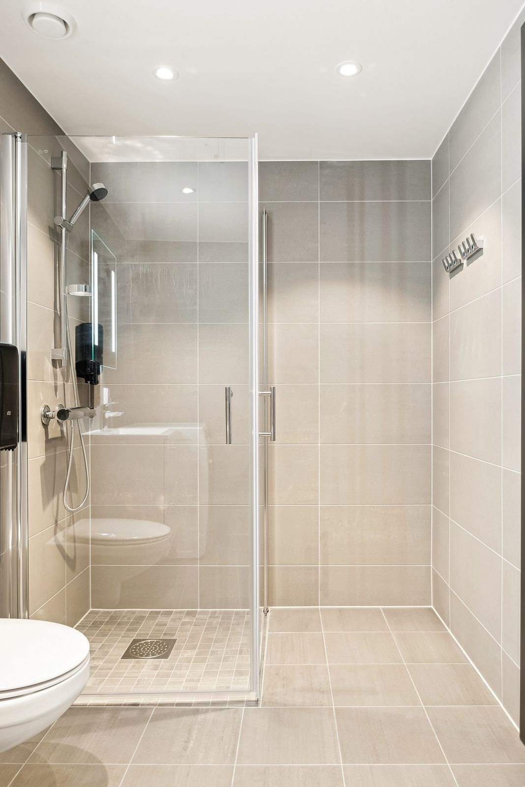 Flislagt baderom med tidløse flisvalg, vegghengt wc og dusjhjørne med praktiske innfellbare dusjvegger i herdet glass. Downlightsbelysning i himling. Galleribilde