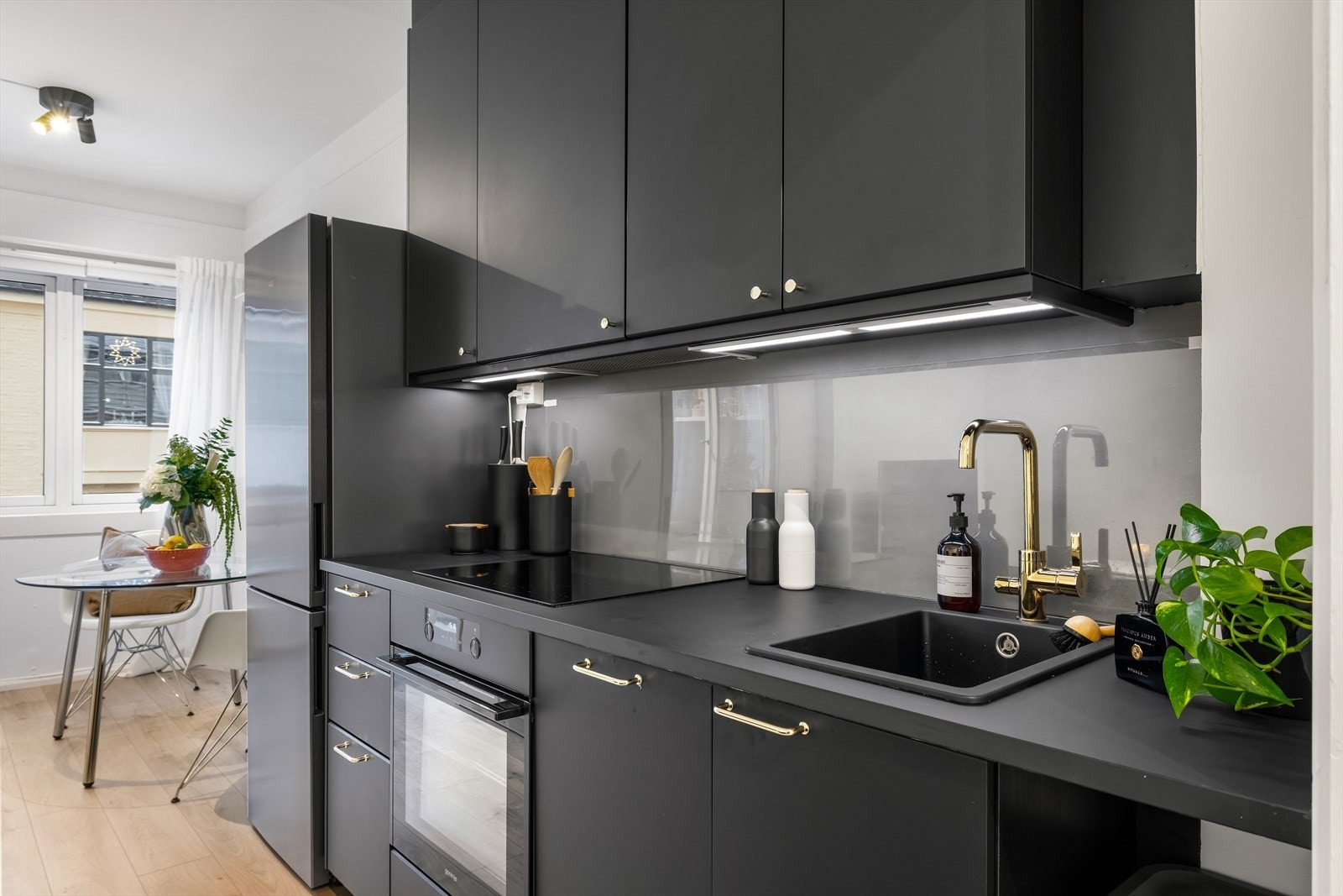 Kjøkkenet fremstår moderne med mørke fronter og helhetlig uttrykk, kombinert med kort vei til spiseplass og godt naturlig lys fra vinduene. Galleribilde