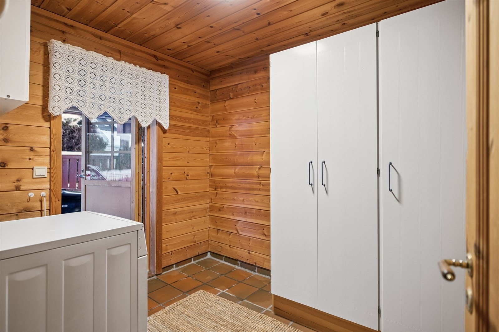 Praktisk vaskerom med flislagt gulv, utslagsvask og opplegg for vaskemaskin. Galleribilde