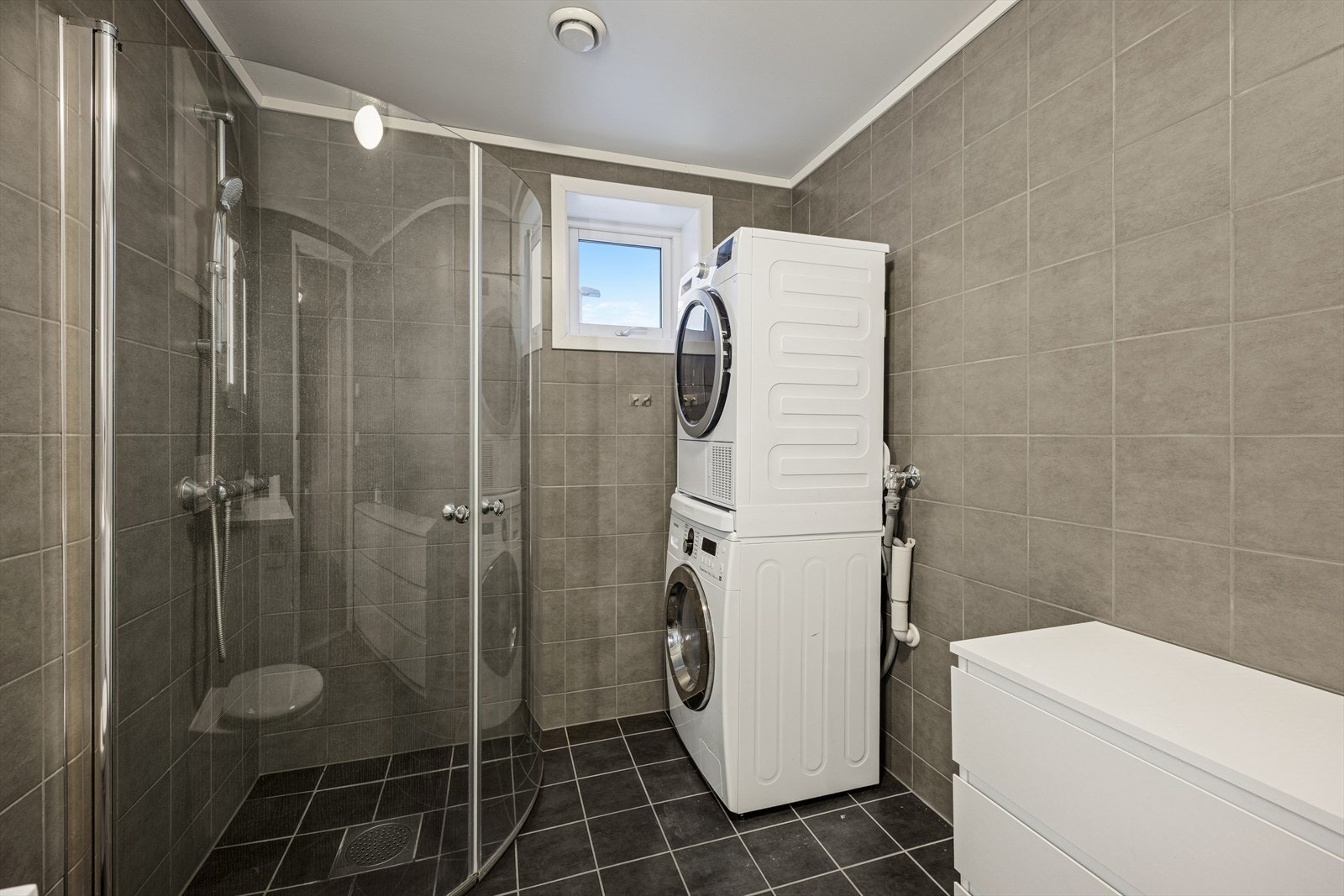 Servantinnredning med skuffer, vegghengt toalett, dusjhjørne med innfellbare vegger og praktisk opplegg for vaskemaskin. Galleribilde