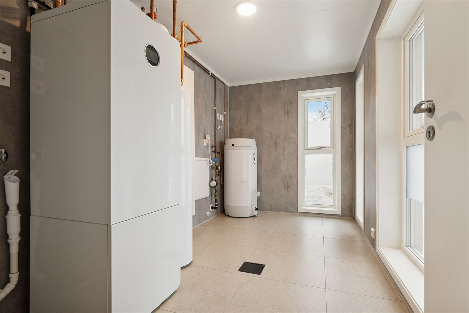 Romslig vaskerom som har praktiske baderomsplater på veggene og flislagt gulv med vannbåren varme. Galleribilde