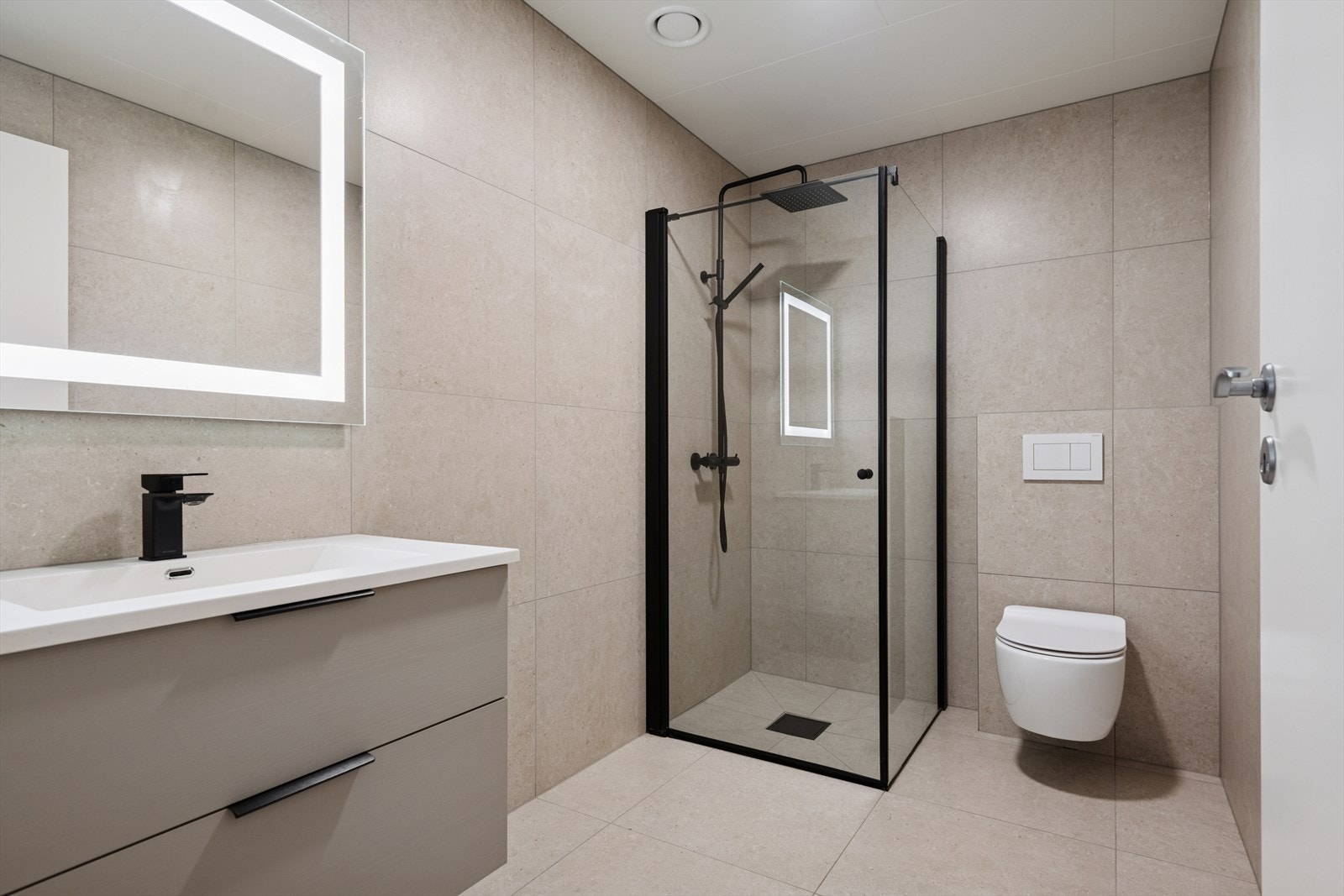 I 1. etasje er det et pent flislagt bad med vannbåren varme i gulvet. Badet er innredet med veggmontert toalett, dusjhjørne med glassvegger, samt innredning med nedfelt servant og speil. Galleribilde