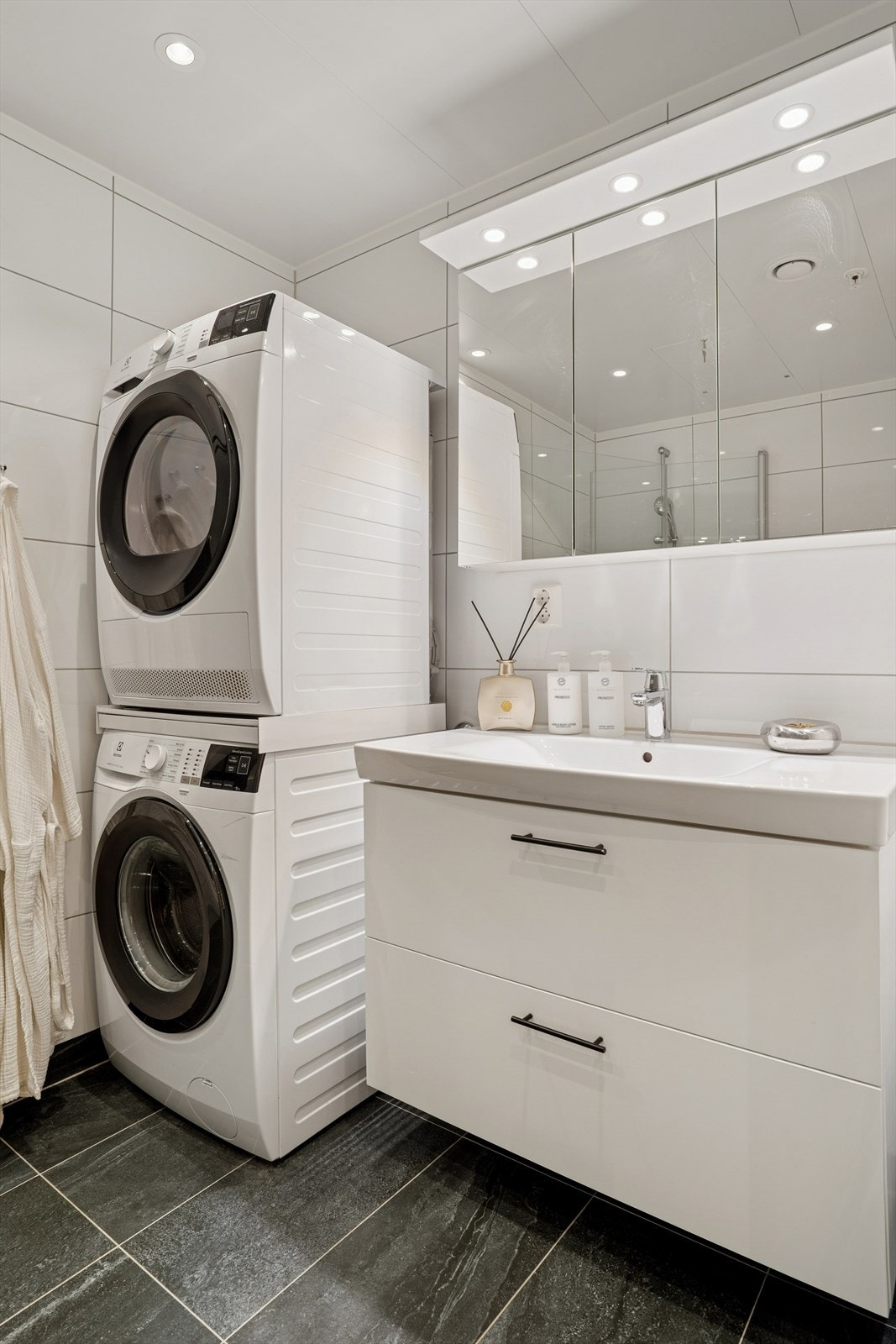 Rommet er utstyrt med servantinnredning, speilskap med lys, vegghengt toalett, dusjhjørne med innfellbare glassdører og opplegg for vaskemaskin. Galleribilde