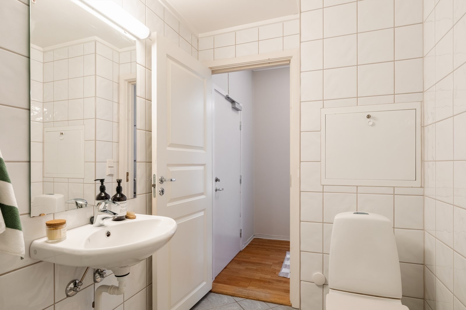 Badet er innredet med gulvmontert toalett, dusjhjørne, veggmontert servant, veggskap med glatte, folierte fronter og speil montert på vegg over servant med tilhørende lysarmatur. Det er opplegg for vaskemaskin. Mekanisk avtrekksventil. Galleribilde