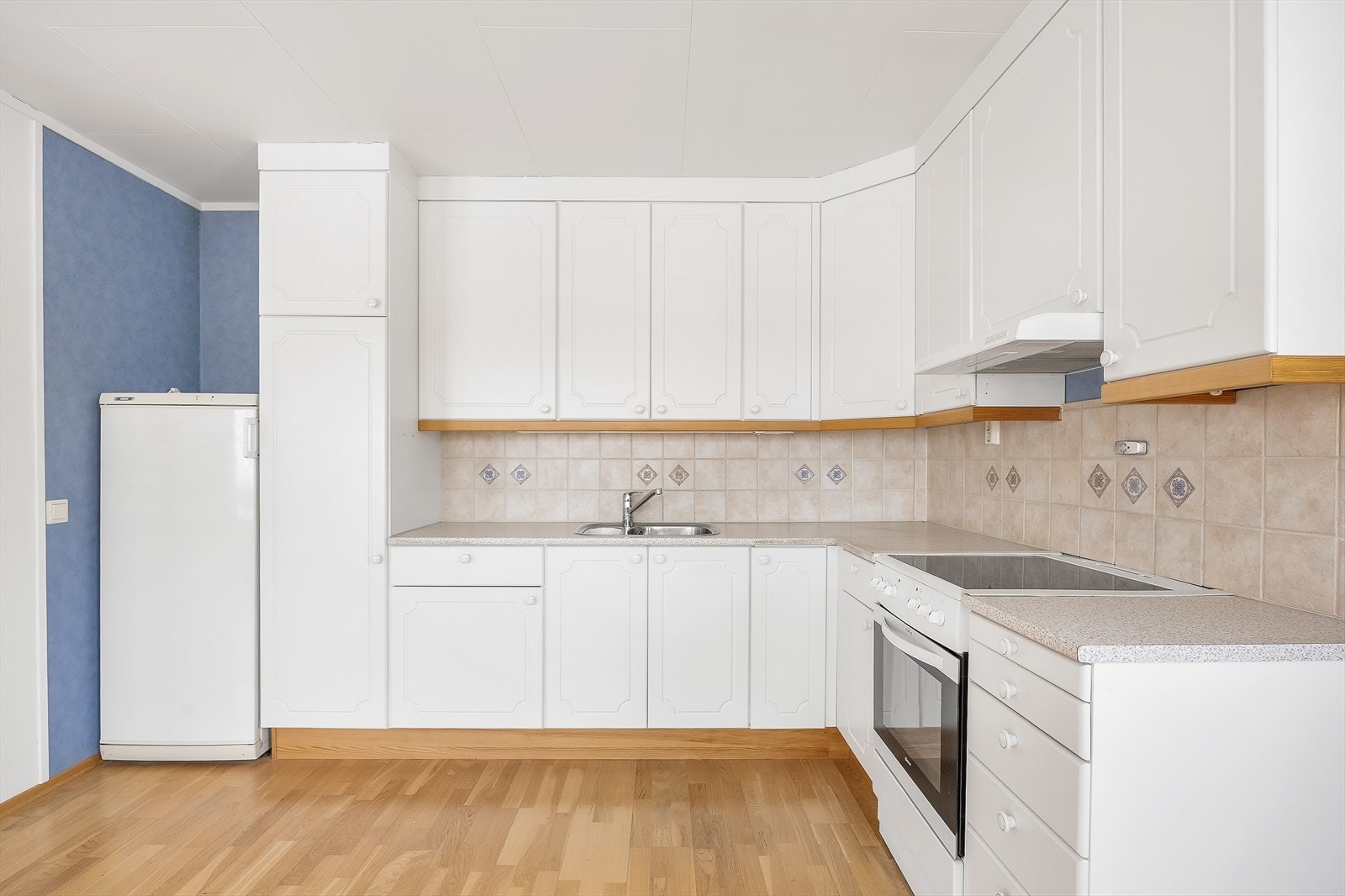 Innredningen er hvit med profilerte fronter, laminat benkeplate og flislagt sprutsone. Galleribilde