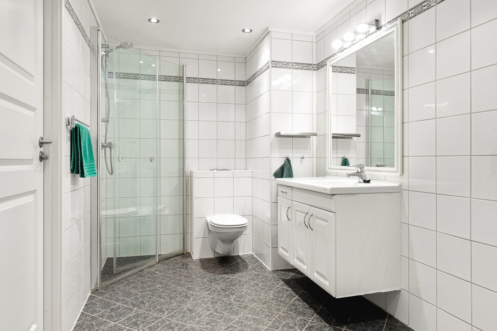 Romslig, helfliset bad med dusj, vegghengt toalett, baderomsinnredning og opplegg for vaskemaskin. Galleribilde