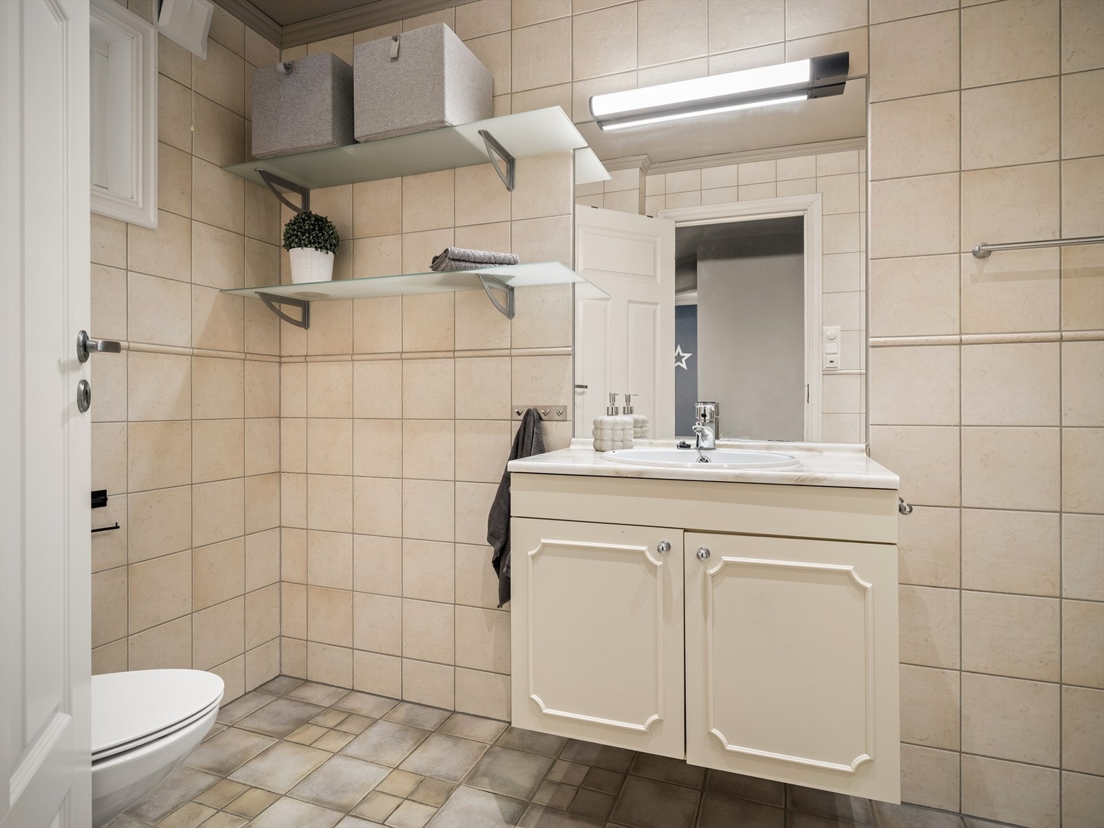 Flislagt bad med servantinnredning og speil med belysning. Galleribilde