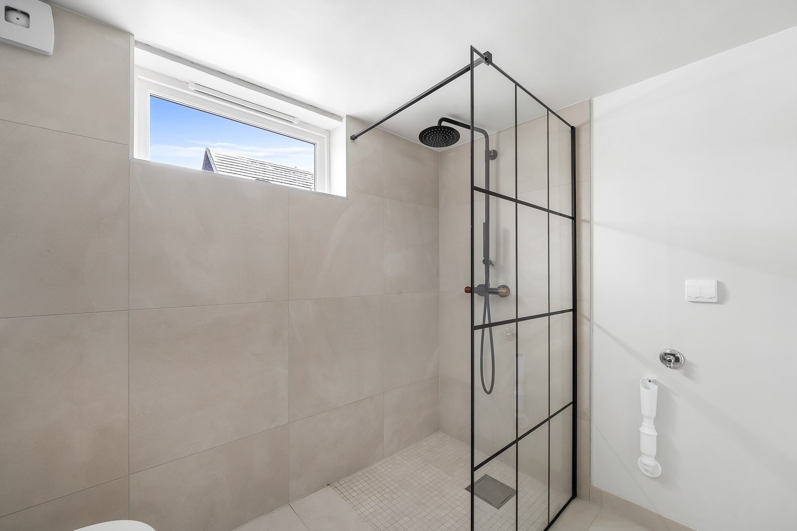 Flislagt bad med vegghengt toalett og dusjnisje med glassvegg. Det er opplegg for vaskemaskin Galleribilde