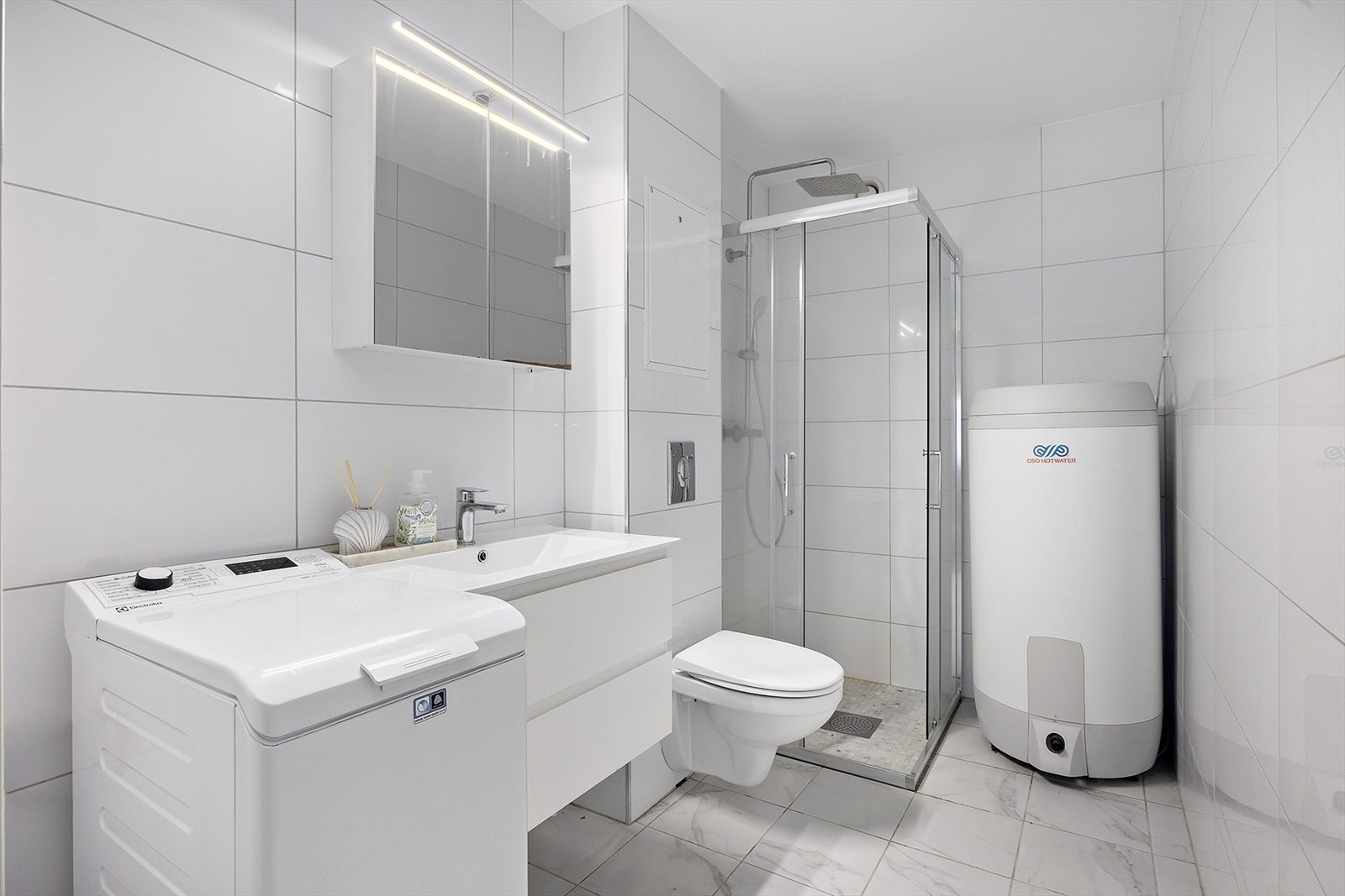 Badet er innredet med servant med innredning, veggmontert toalett, dusjhjørne med glassvegger samt opplegg for vaskemaskin. Galleribilde