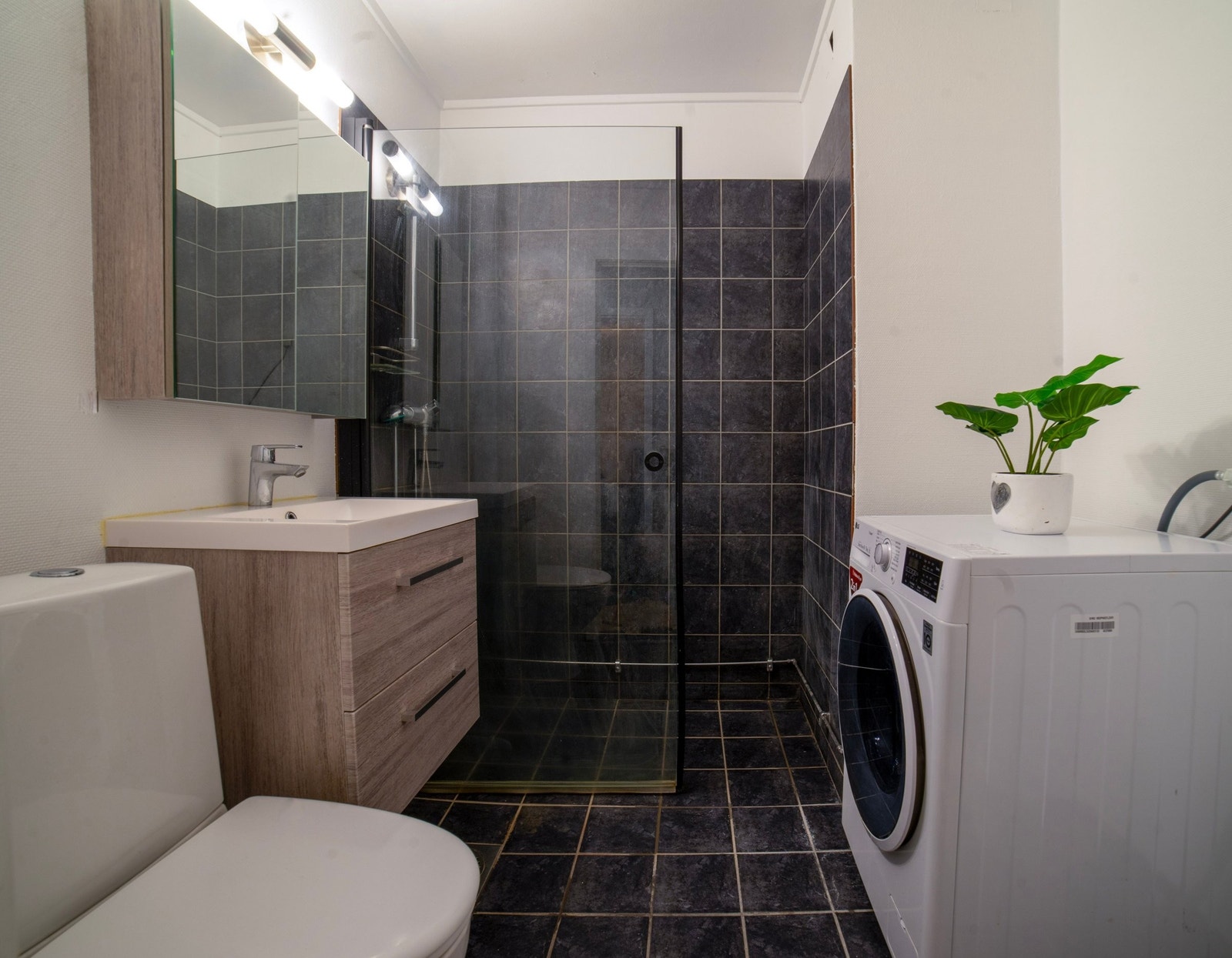 Flislagt bad utstyrt med dusjhjørne, servant med oppbevaring og opplegg for vaskemaskin. Kombinert vaskemaskin/tørketrommel fra 2020 følger med leiligheten. Galleribilde