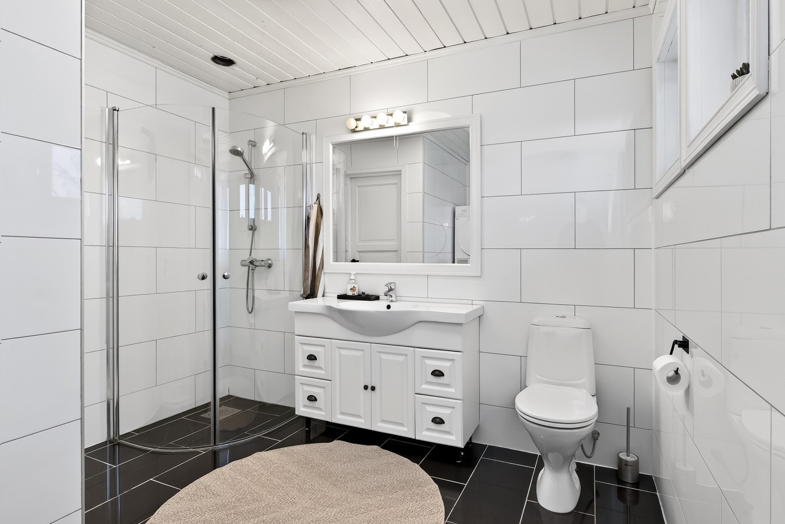 Tidløst bad med fliser på vegg og gulv, gulv med behagelig gulvvarme, dushjørne med dører og servantinnredning med skuffer og dører. Galleribilde