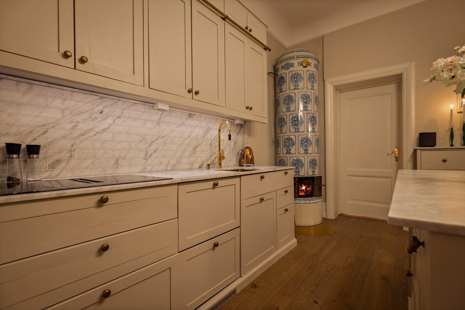 Kakkelovnens tidløse tilstedeværelse løfter rommet og binder sammen kjøkkenets klassiske og moderne elementer. Galleribilde