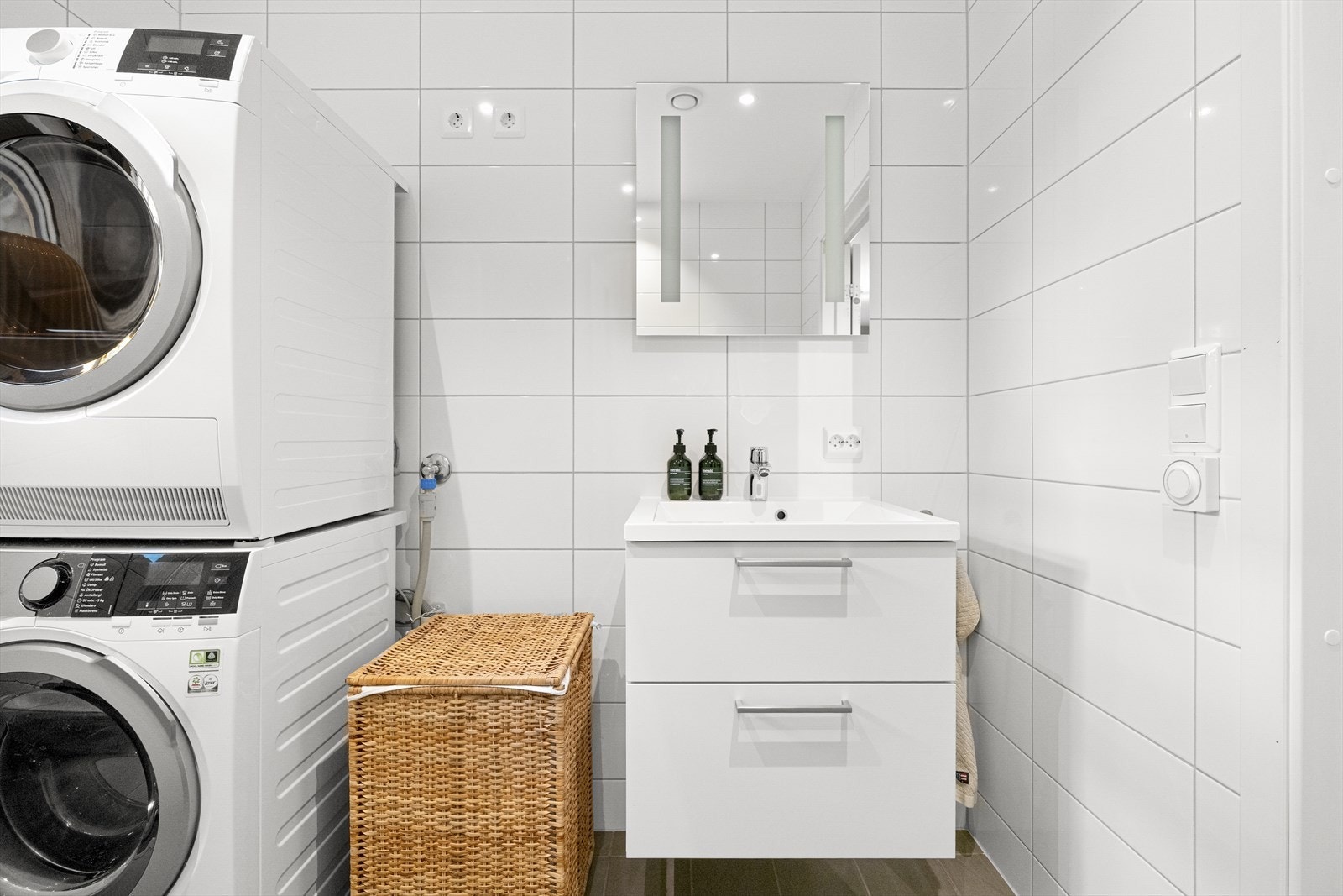 Innredet med nedfelt servant i baderomsmøbel, veggmontert toalett og dusjhjørne, samt opplegg for vaskemaskin og tørketrommel. Galleribilde