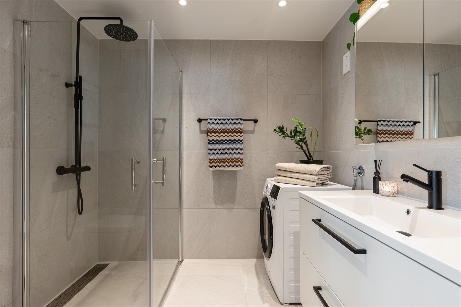 Delikat, flislagt bad med dusjhjørne, vegghengt toalett og opplegg for vaskemaskin. Galleribilde