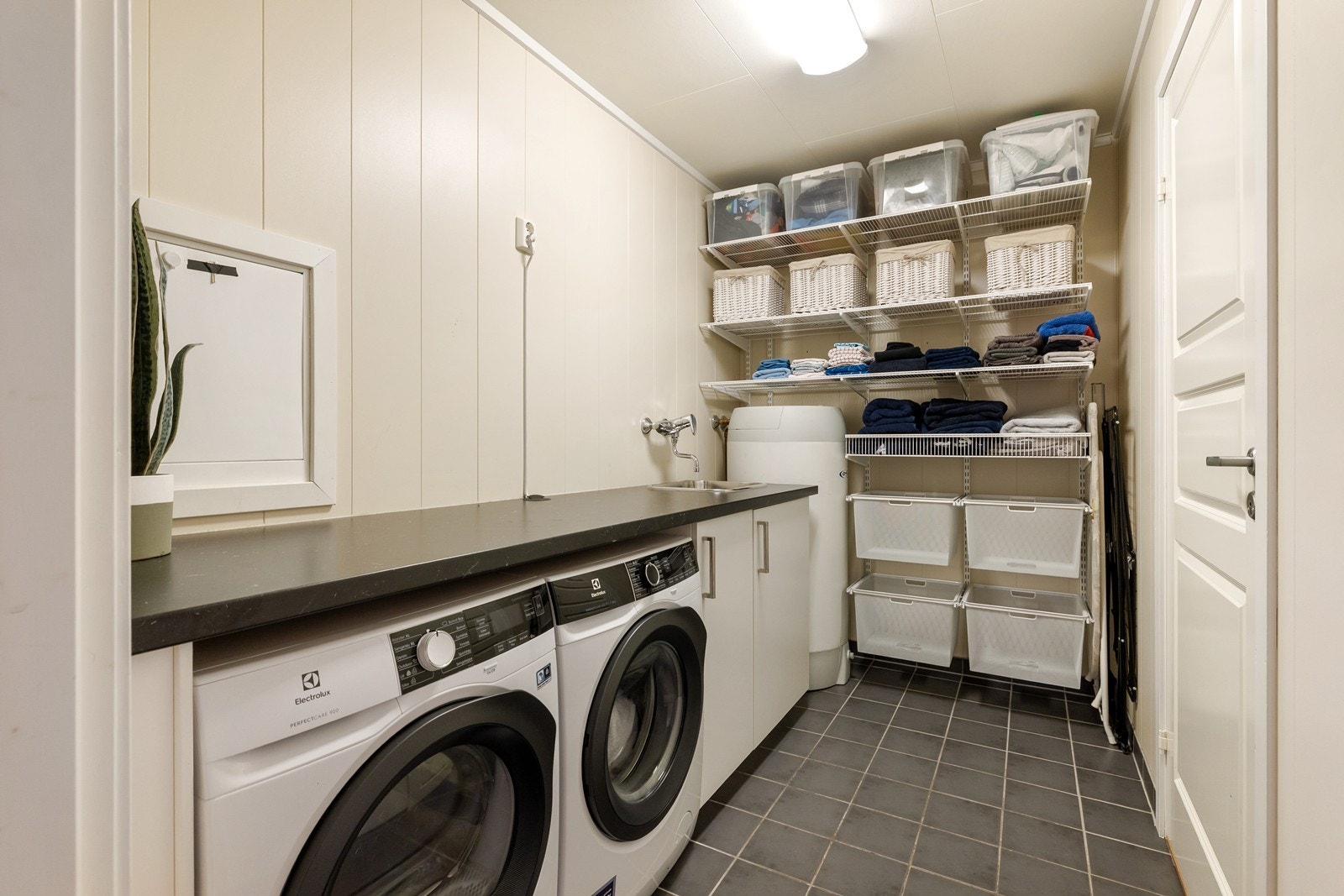 Meget praktisk vaskerom med flislagt gulv og oppbevaringsinnredning på vegg. Galleribilde