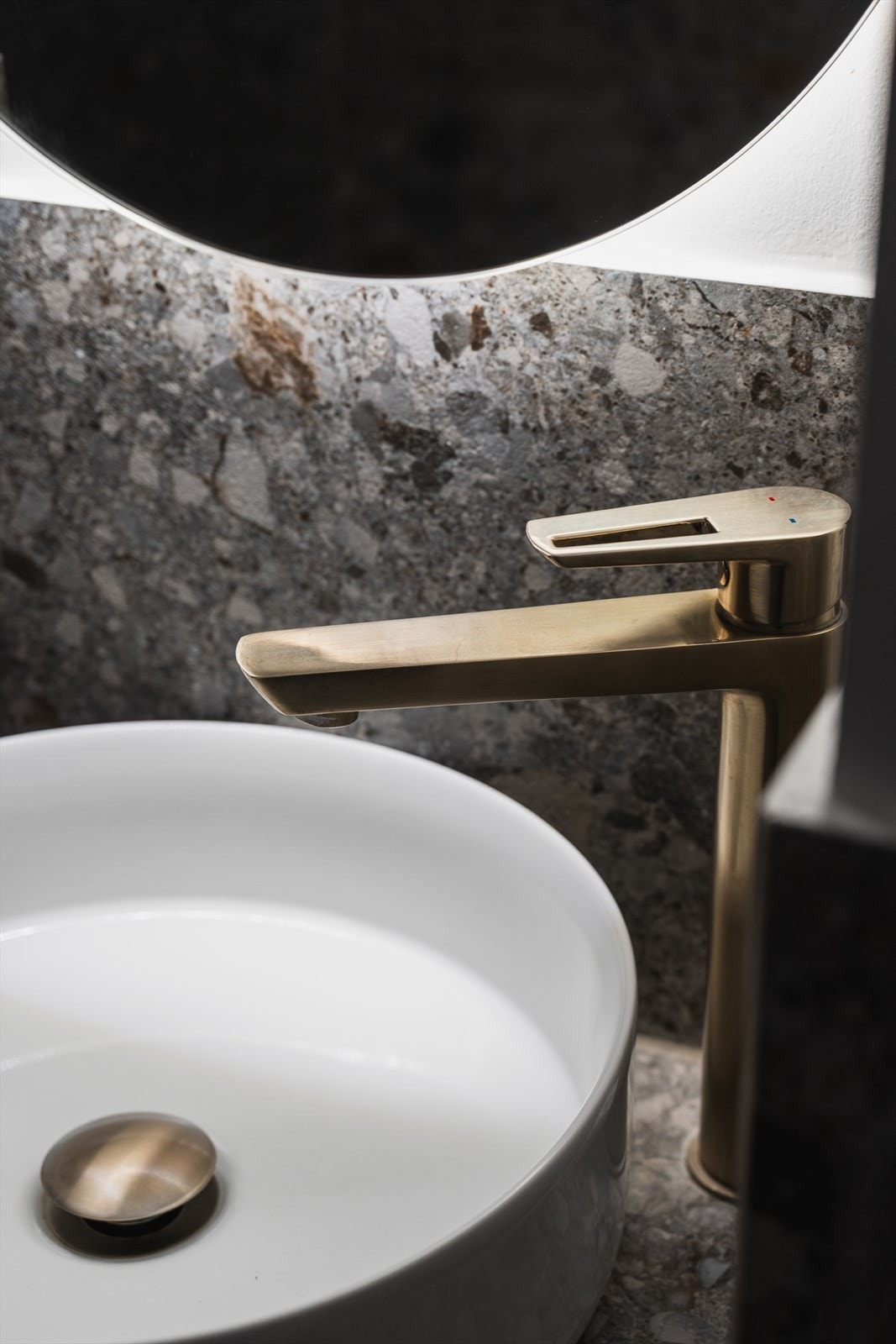 Badet er innredet med servant på flislagt benk, speil med lysarmatur og veggmontert klosett. Ventilasjon består av elektrisk avtrekksvifte i himling og små luftehull i dør. Galleribilde