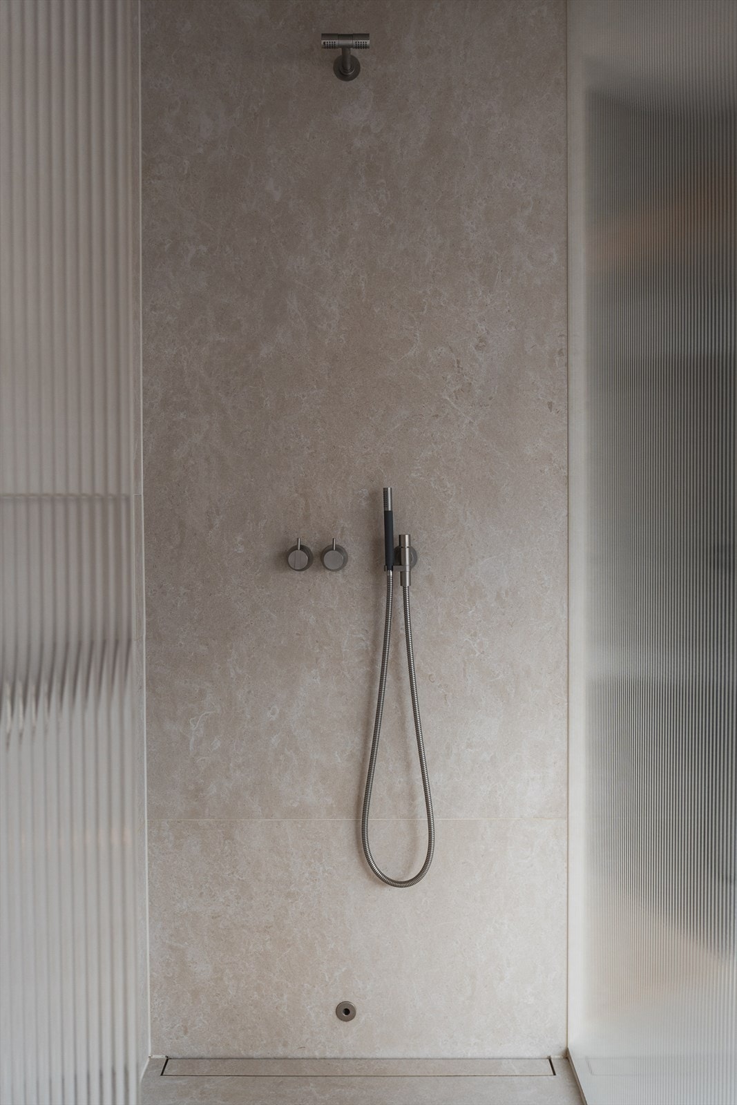 Det er et nedsenket dusjhjørne med glassvegg, rennesluk, regnfallsdusj og termostatstyrt blandebatteri fra Vola Galleribilde