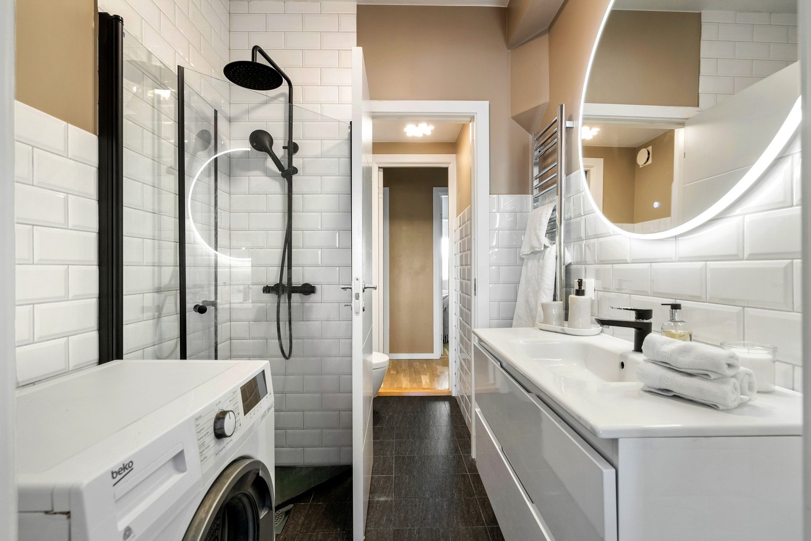 Leilighetens baderom har lyse fliser og varme på gulv, og lyse fliser kombinert med malte flater på vegger. Galleribilde