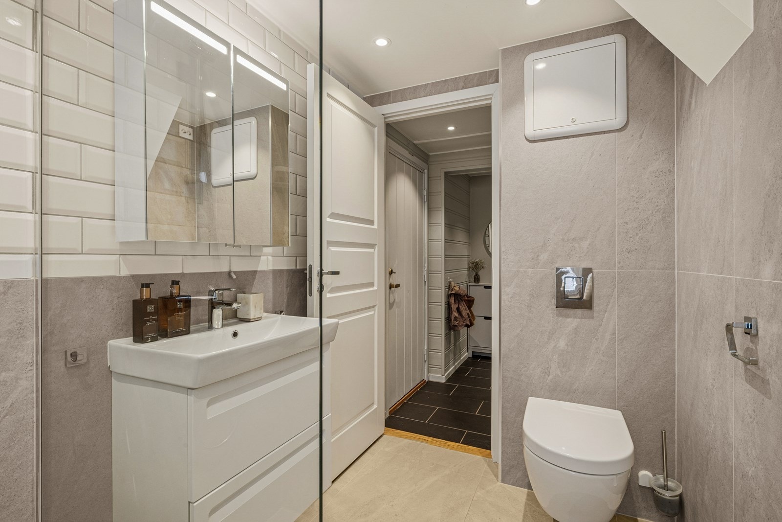 Badet er utstyrt med vegghengt toalett, servant med servantskap, speilskap og dusj. Galleribilde