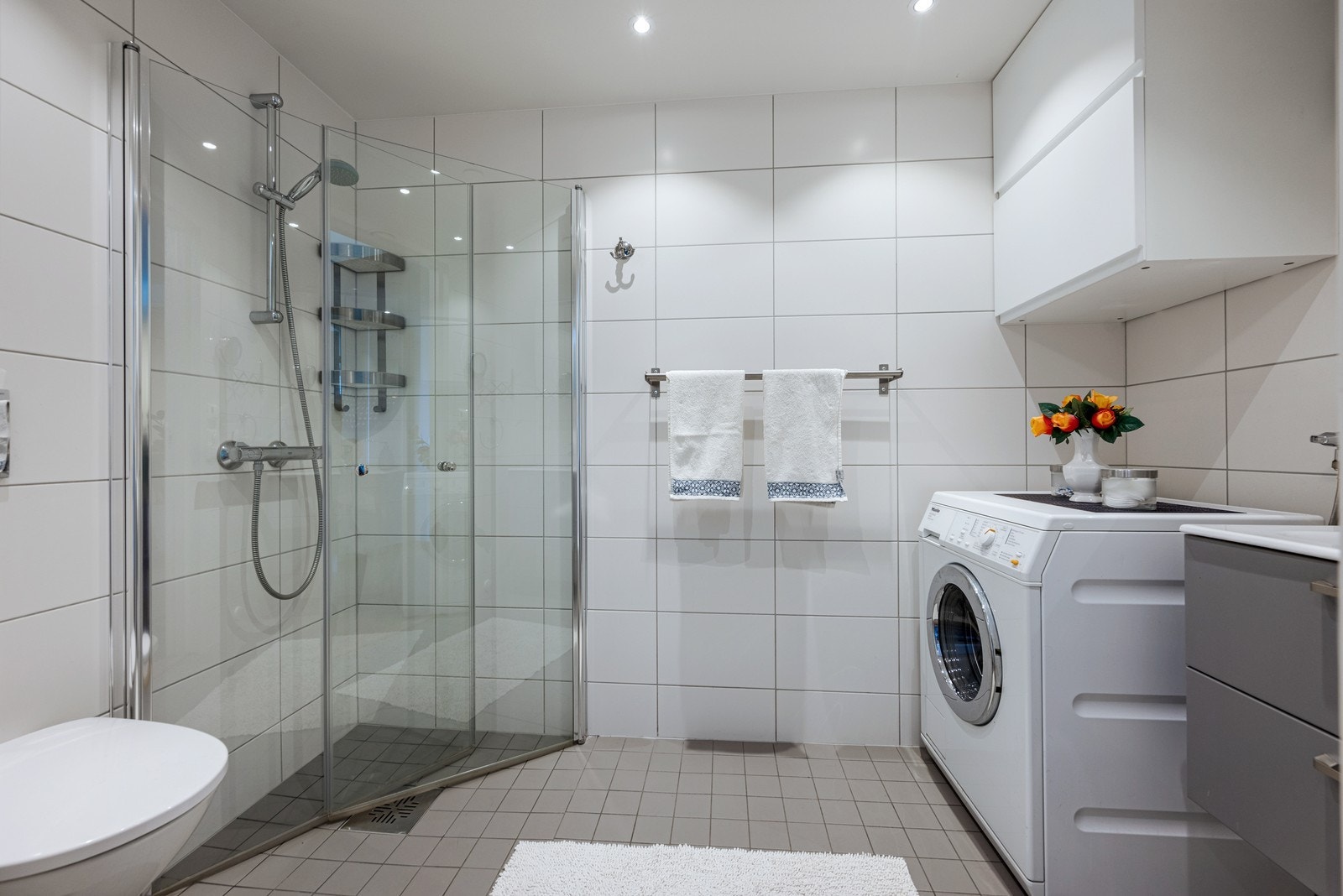 Pent flislagt bad med innfellbare dusjdører og vaskemaskin. Galleribilde