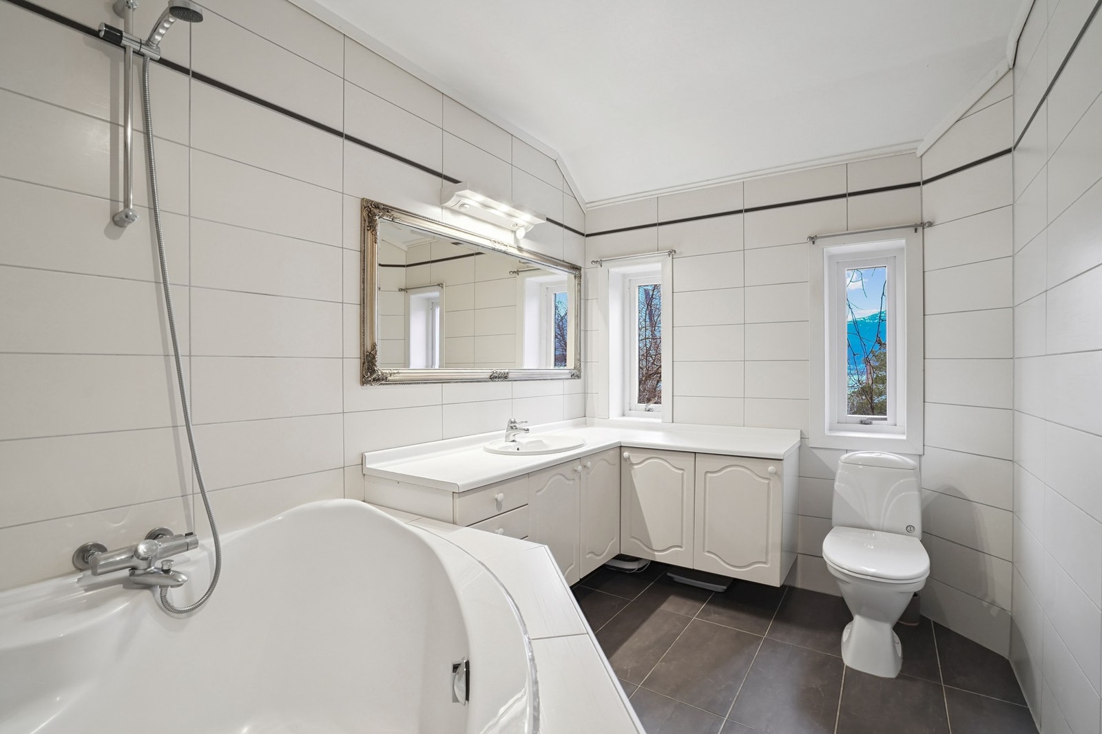 Baderom har innredning med profilerte fronter. Benkeplate med nedfelt servant. Speil og belysning over. Galleribilde