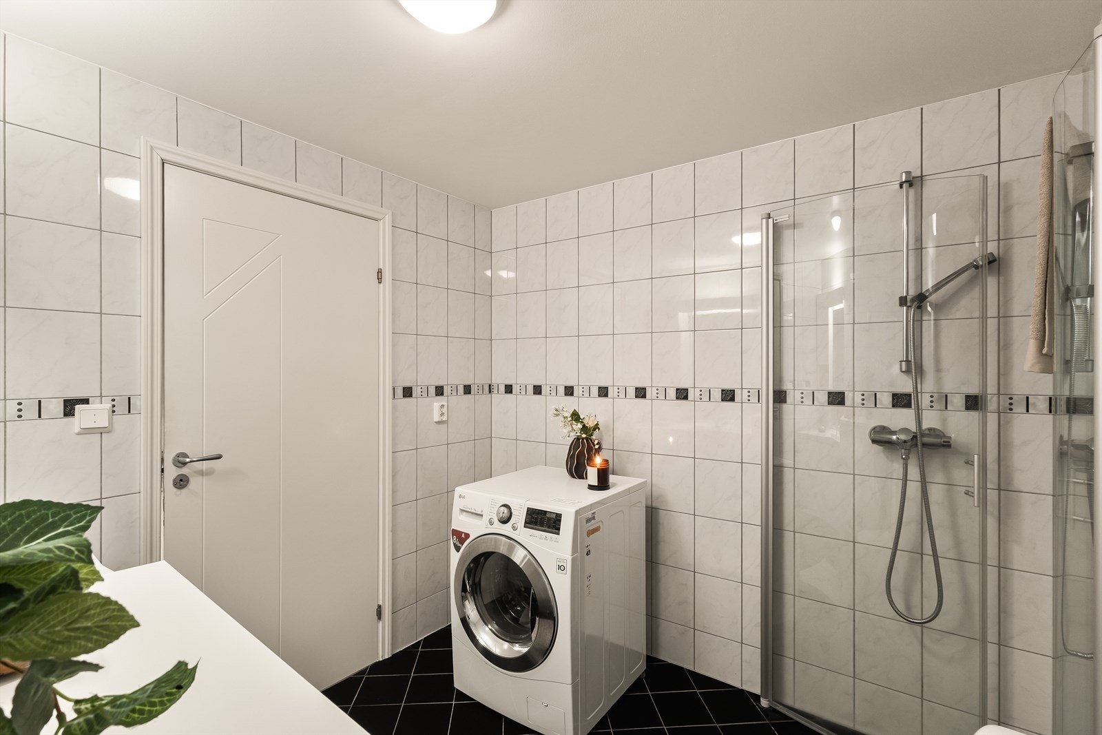 Vegger er belagt med lyse fliser, mens gulv har mørkere fliser som gir en fin kontrast. Det er opplegg for vaskemaskin. Galleribilde