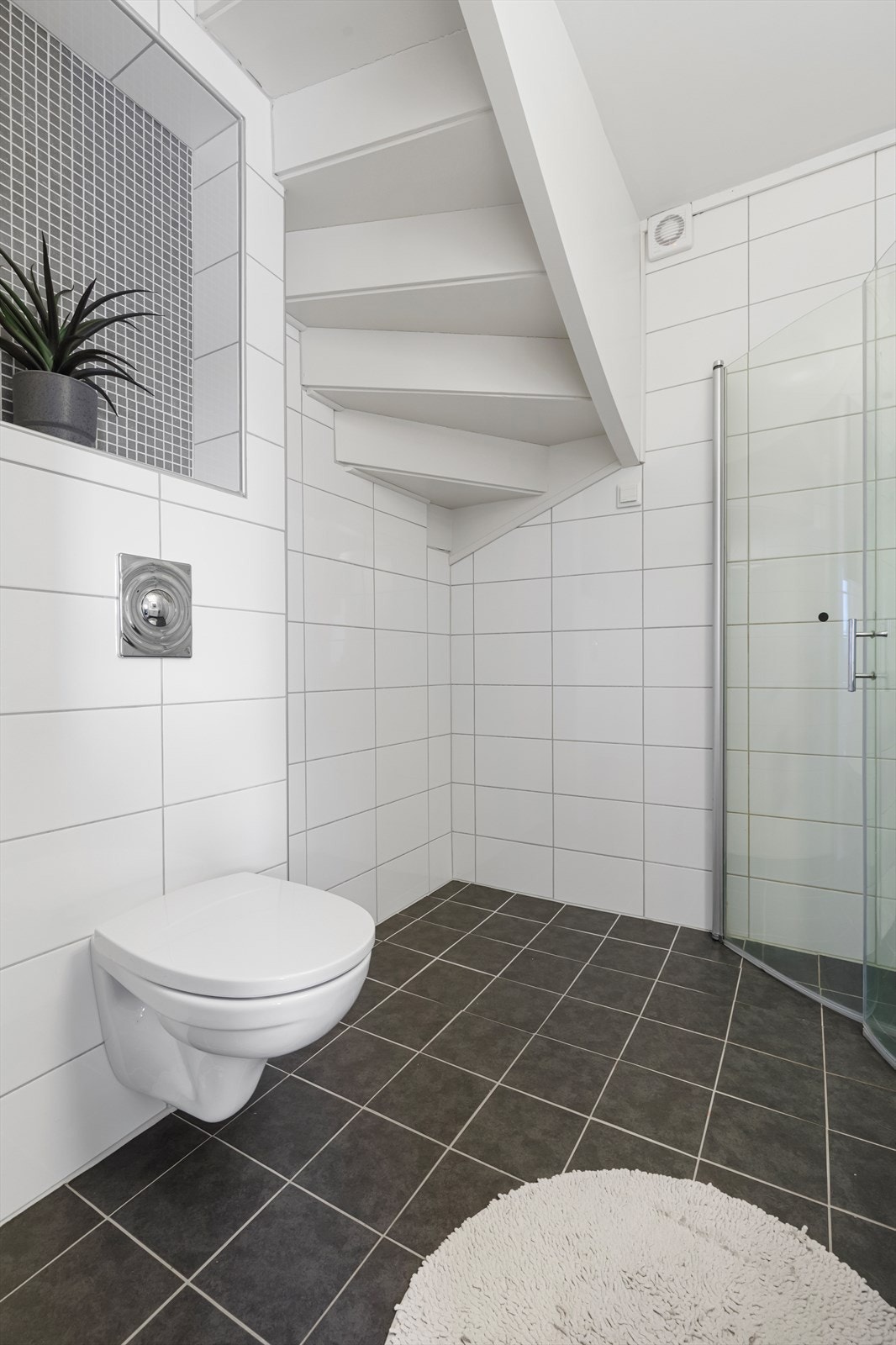 Bad i 1. etasje har flislagt gulv og vegger og er utstyrt med vegghengt wc, vegghengt dusj med dusjvegger og baderomsinnredning Galleribilde