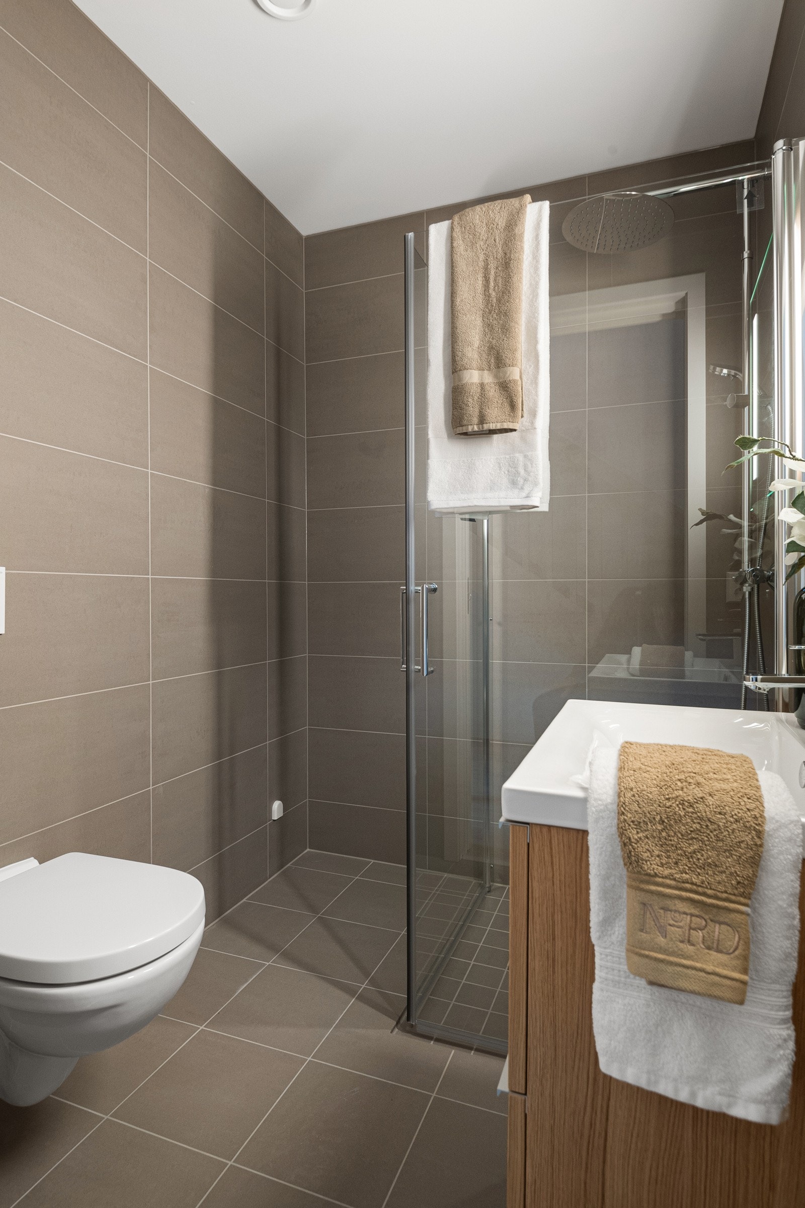 Badet i kjelleren er helfliset og moderne, med dusjhjørne i glass, vegghengt toalett og servantskap. Varmekabler i gulv gir god komfort. Galleribilde