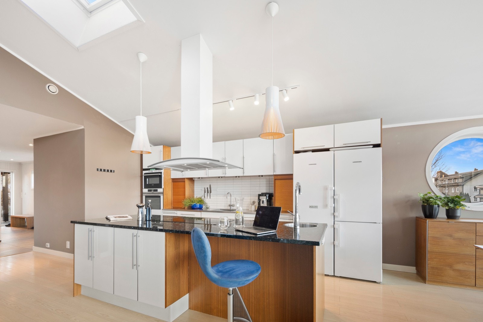 Kjøkkeninnredningen har slette høyglans lakkerte fronter, benkeplate i stål med kum og fliser på veggen over kjøkkenbenken Galleribilde