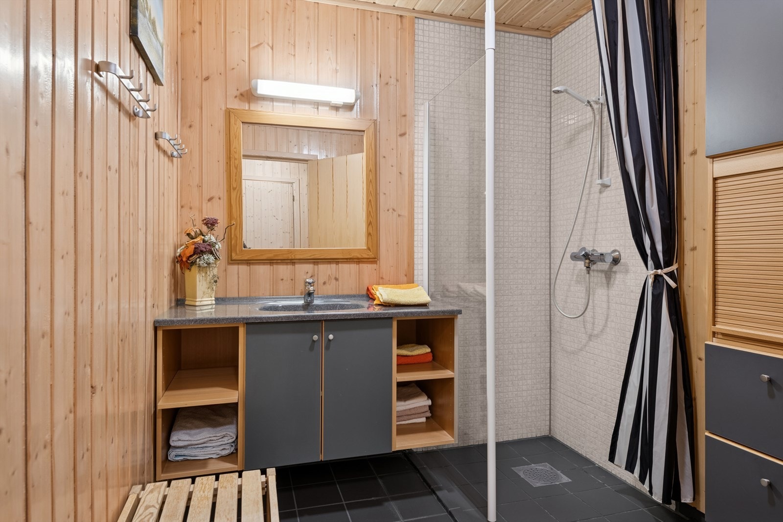 Bad er fra byggeår. Veggene har panel, fliser i dusjsonen. Gulvet er flislagt. Rommet har innredning med nedfelt servant, toalett og dusjvegger/hjørne. Balansert ventilasjon. Galleribilde