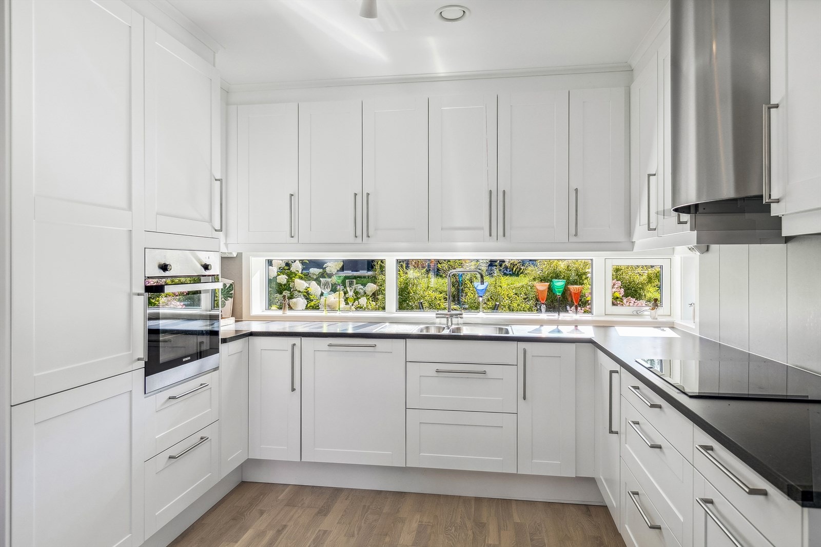 Kjøkkeninnredningen har profilerte fronter, integrerte hvitevarer og benkeplate i høytrykkslaminat. Detaljer i krom. Galleribilde