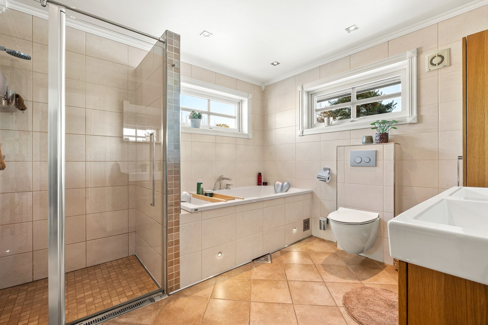 Badet i 1. etasje er flislagt med varmekabler i gulv. Dusjhjørne, vegghengt wc og badekar. Dobbel servant i innredningen. Galleribilde