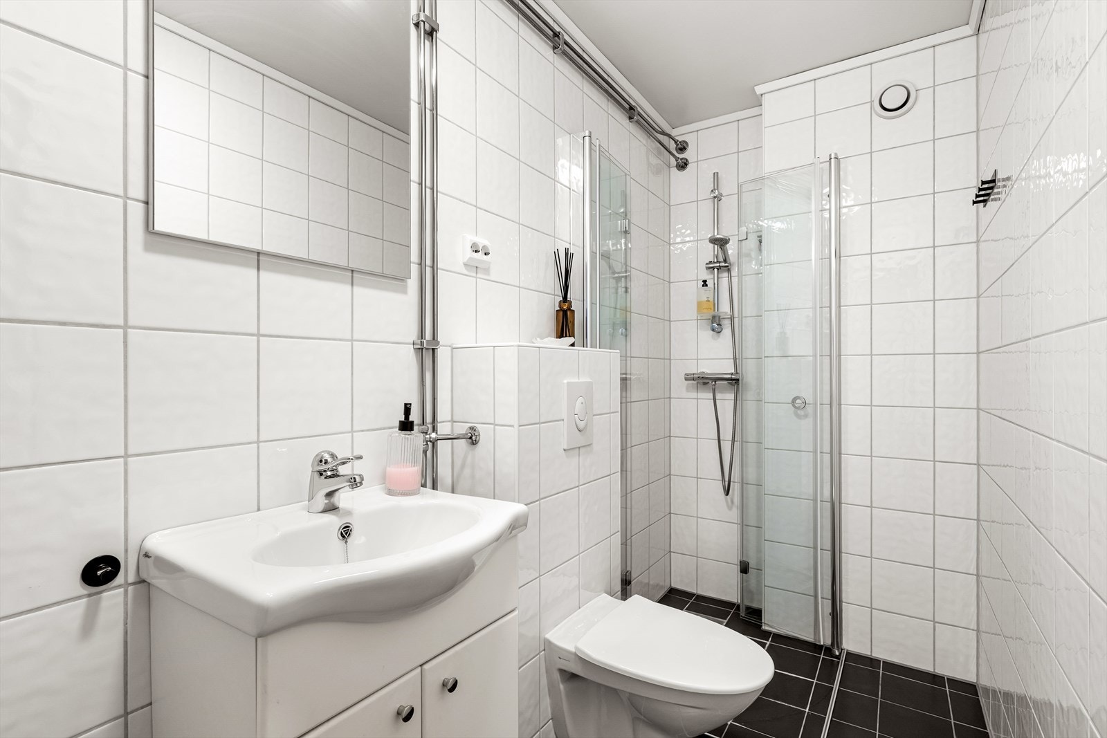 Flislagt bad med dusjhjørne, servant med underskap og vegghengt toalett Galleribilde