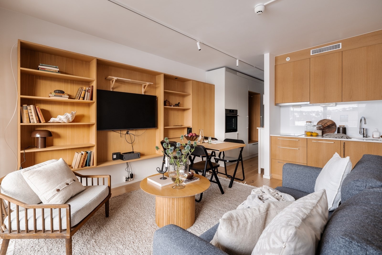 Rommet er innredet med en spesialtilpasset veggseksjon med åpen hylleplass, TV-løsning og et nedfellbart spisebord. Bordet gir plass til måltider for fire og kan enkelt slås opp når det ikke er i bruk. Galleribilde