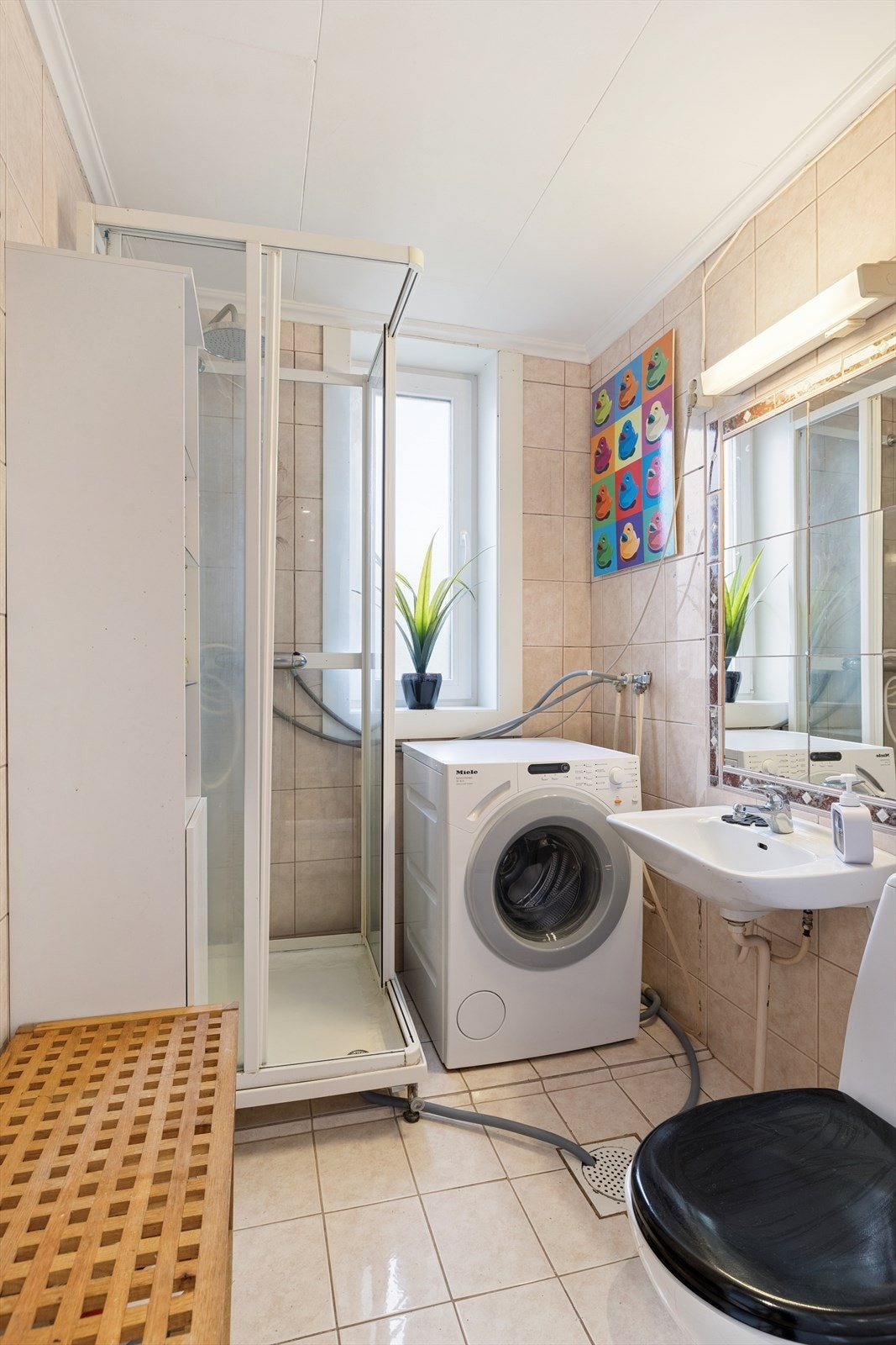 Badet er helfliset og inneholder toalett, dusjkabinett, baderomsinnredning og opplegg for vaskemaskin. Galleribilde