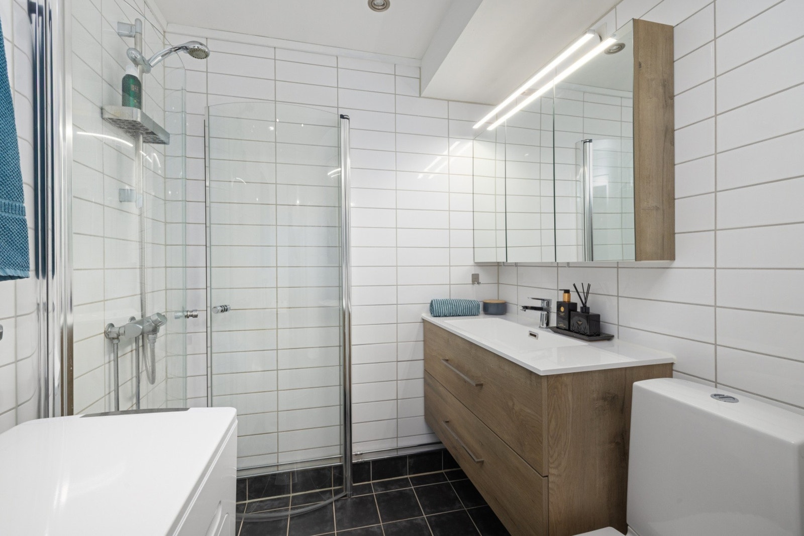 Moderne, flislagt bad med dusj, pen innredning og opplegg for vaskemaskin. Galleribilde