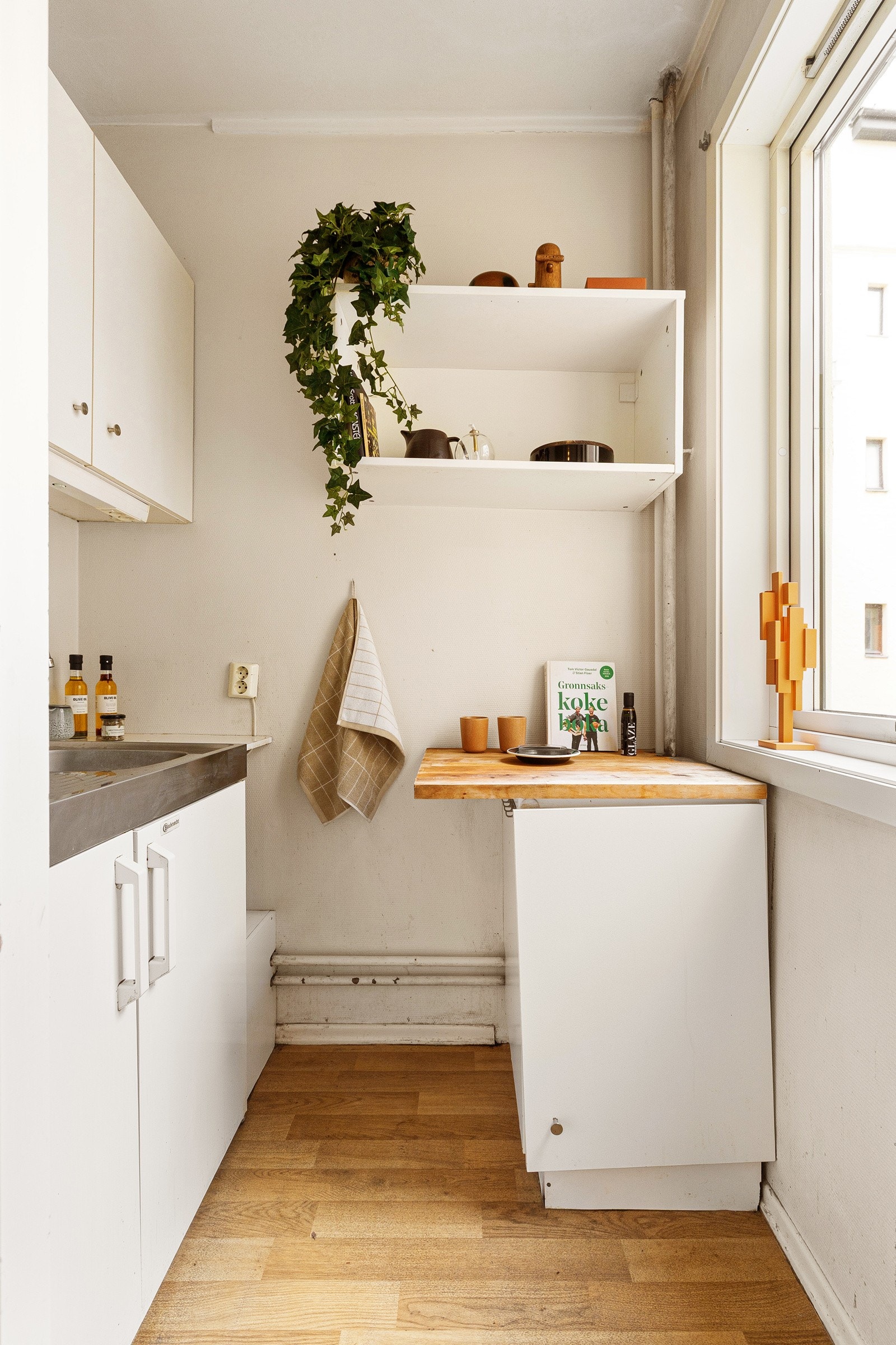 T-kjøkken med hvite fronter og vaskekum med to koketopper. Suplert med småskap med hvite fronter og benkeplate i heltre Galleribilde