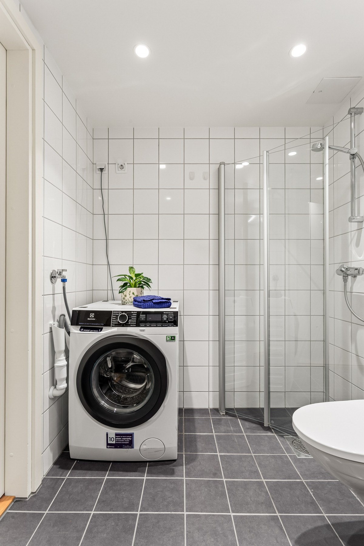 Videre inneholder baderommet et dusjhjørne med svingdører i glass, veggmontert klosett og opplegg for vaskemaskin. Galleribilde